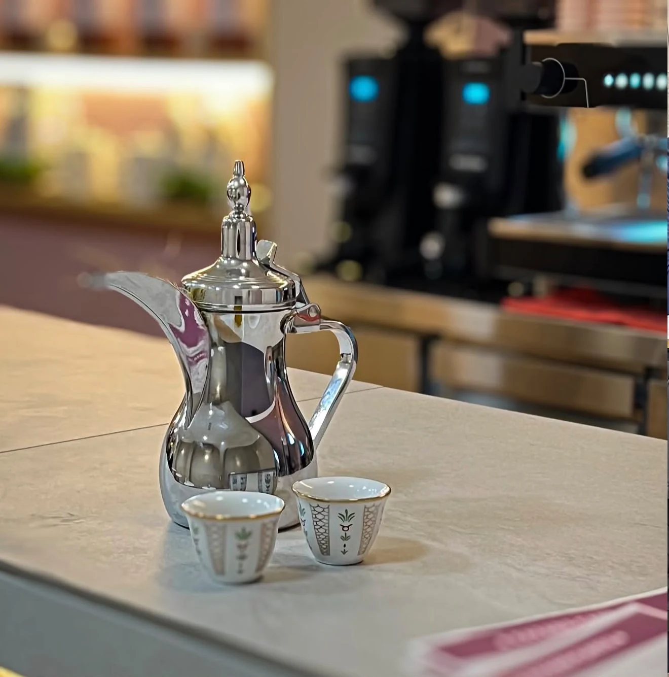 Cafetera árabe plateada y dos tazas sobre una mesa